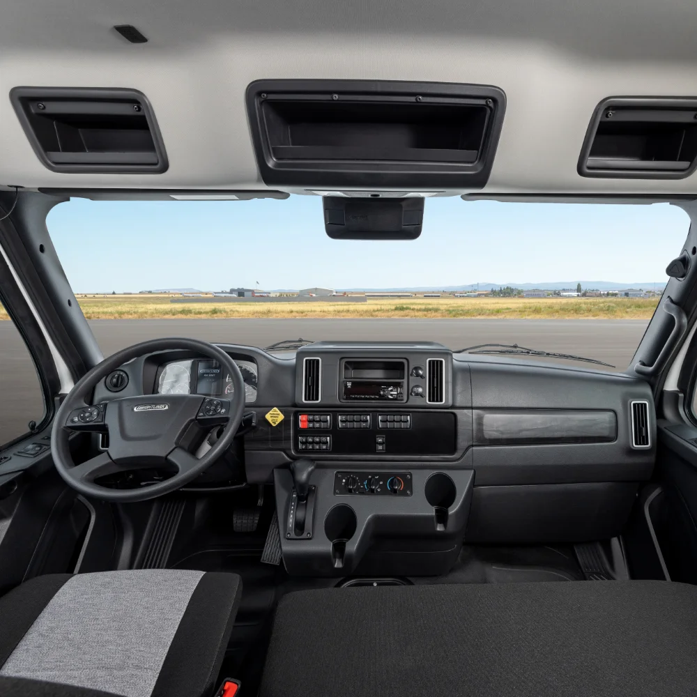 Interior view of Freightliner m2106 plus truck cabin with steering wheel, dashboard, and clear view of the airstrip